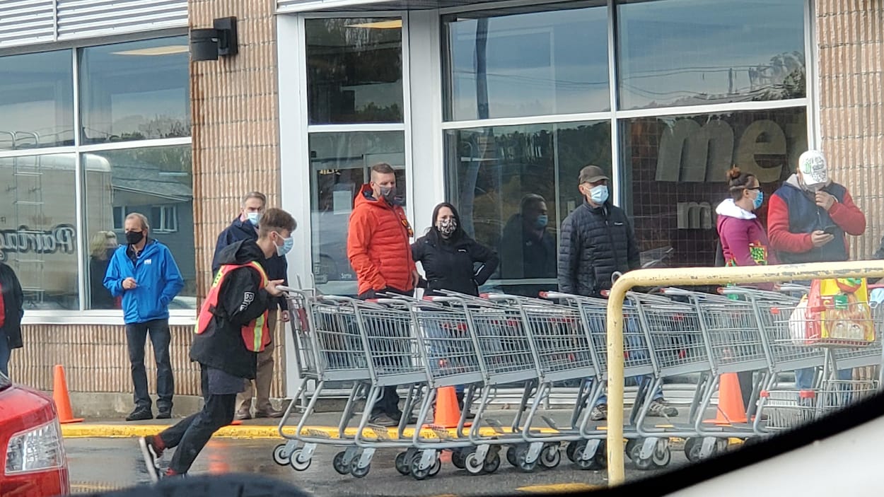 Des personnes masquées font la file à l'extérieur de l'épicerie.