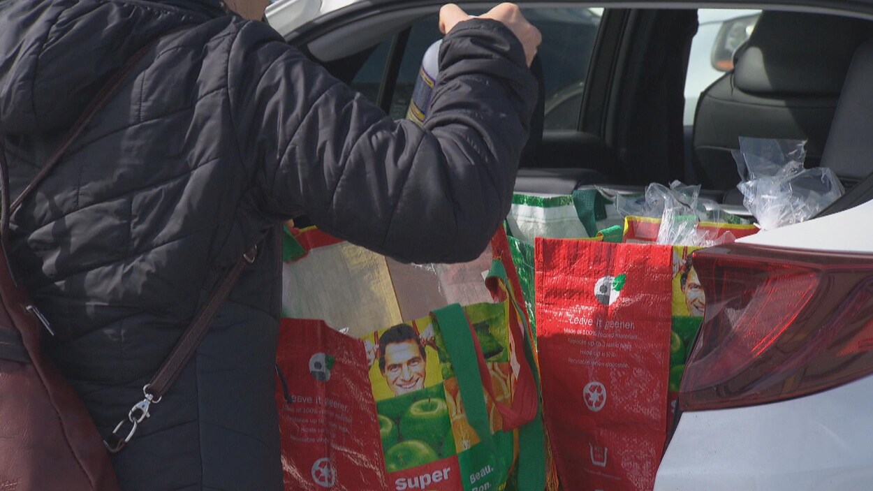 Une femme dépose quelque chose dans les sacs d'épicerie réutilisable qui se trouvent dans le coffre de sa voiture.