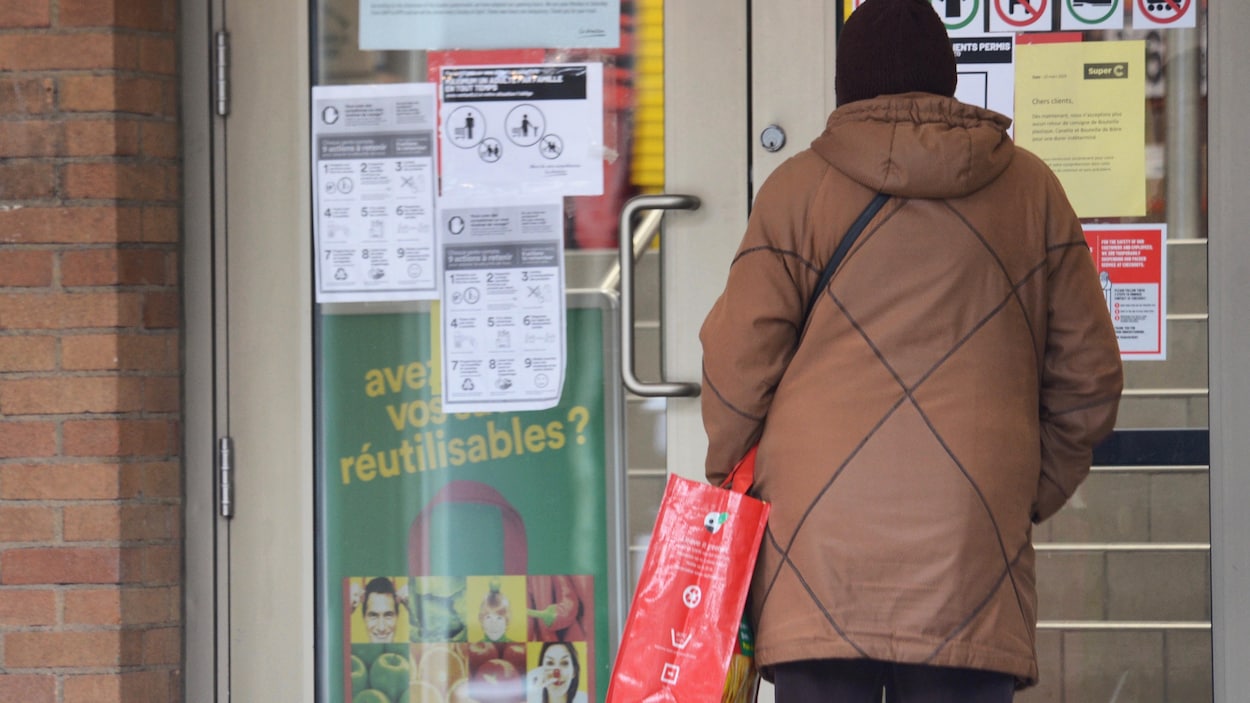 Une dame debout devant la porte fermée d'une épicerie