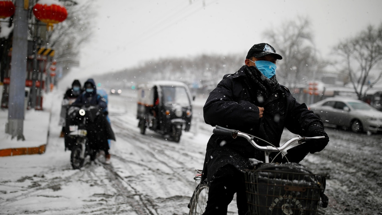 Un homme en moto sous la neige à Pékin avec un masque au visage.