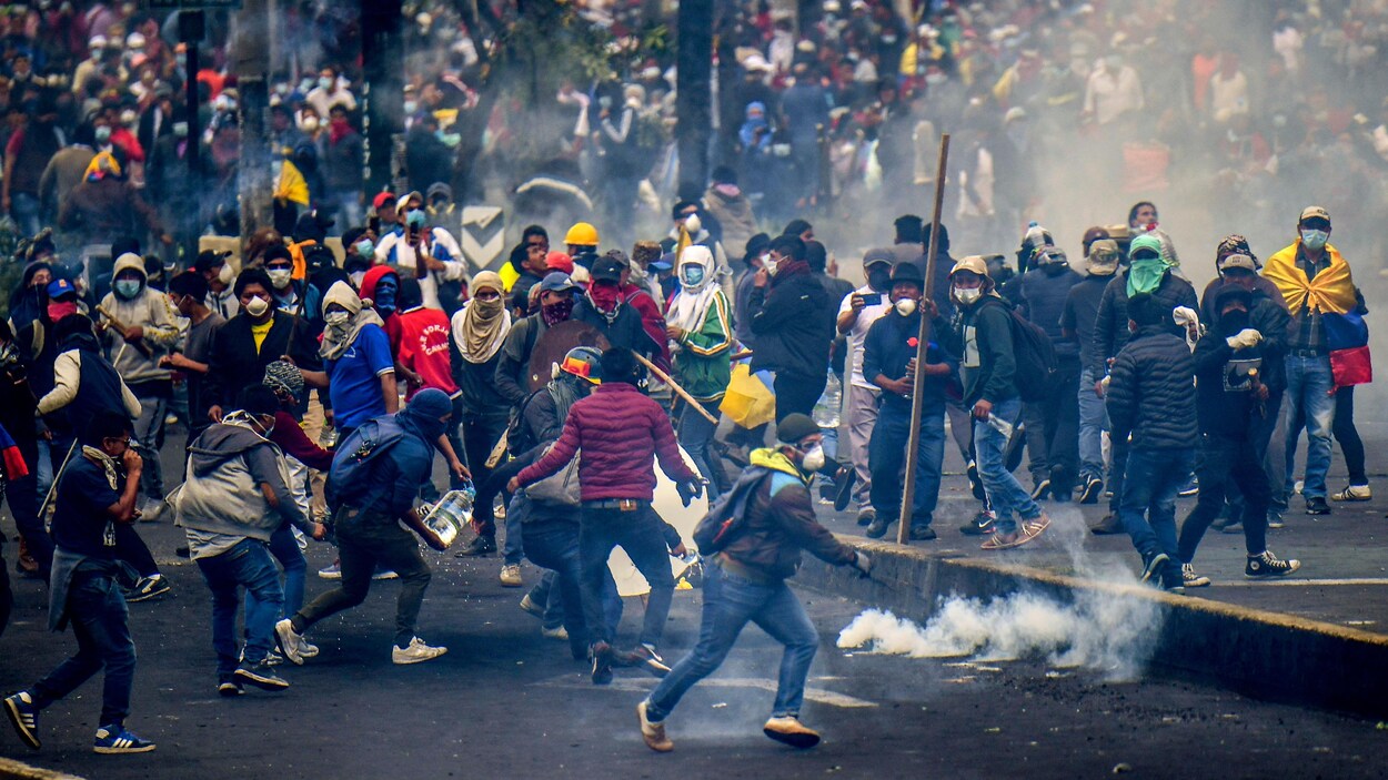 Des centaines de personnes masquées manifestent, des bombes de gaz lacrymogène à leurs pieds.