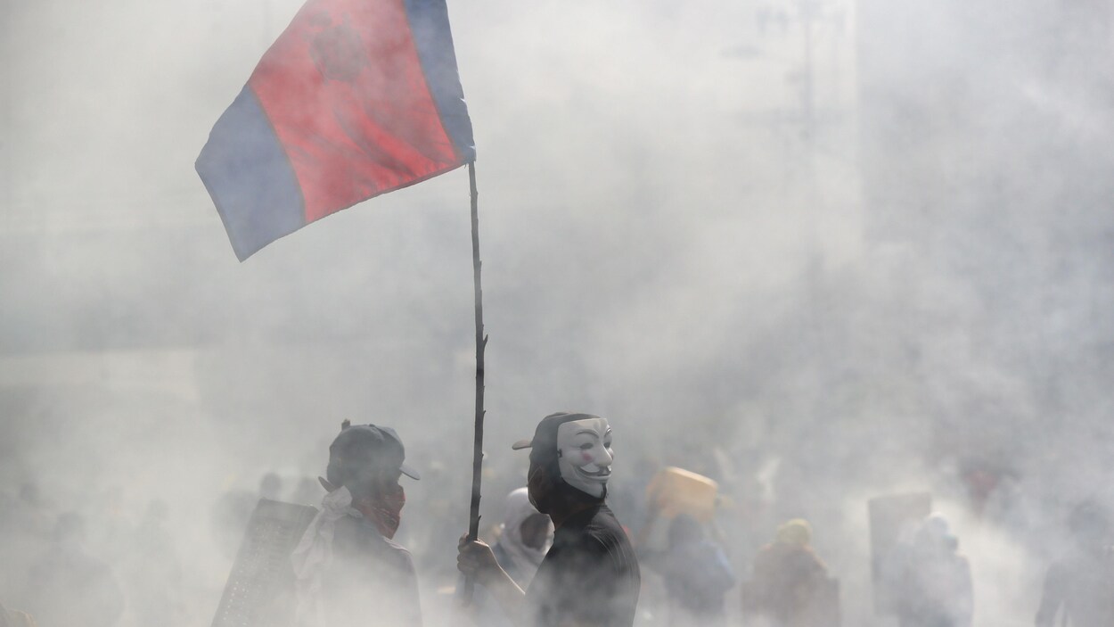 Un manifestant, vêtu d'un masque de Guy Fawkes, dans une rue de Quito obscurcie par les fumées lacrymogènes.