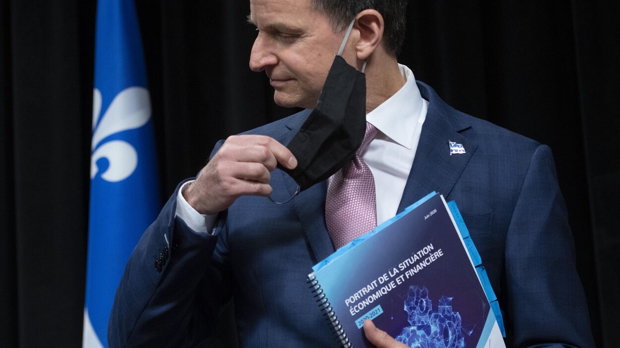 Le ministre enlève son masquet tient un document intitulé « Portrait de la situation économique et financière 2020-2021 ».