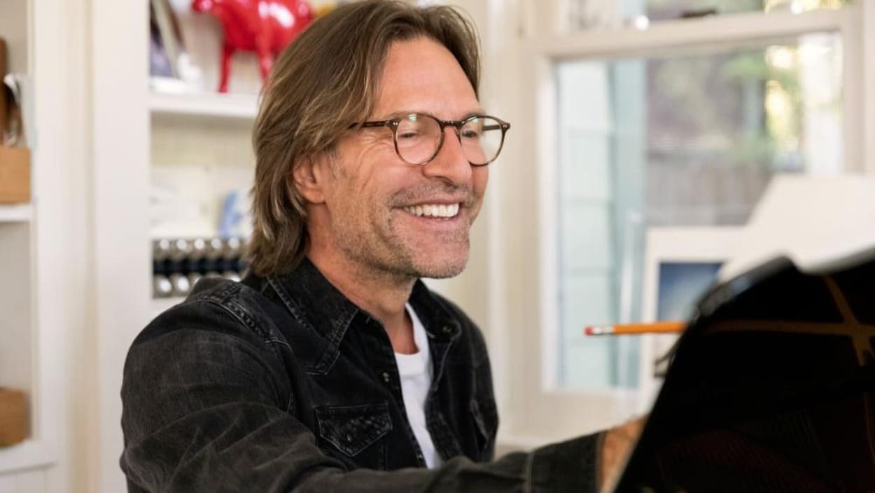 Eric Whitacre est au piano et il sourit.