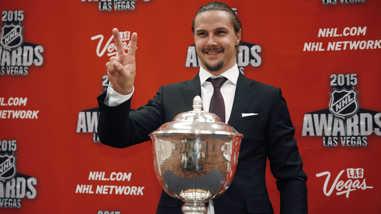 Erik Karlsson salue les caméras en se tenant derrière un trophée. Erik Karlsson salue les caméras en se tenant derrière un trophée.