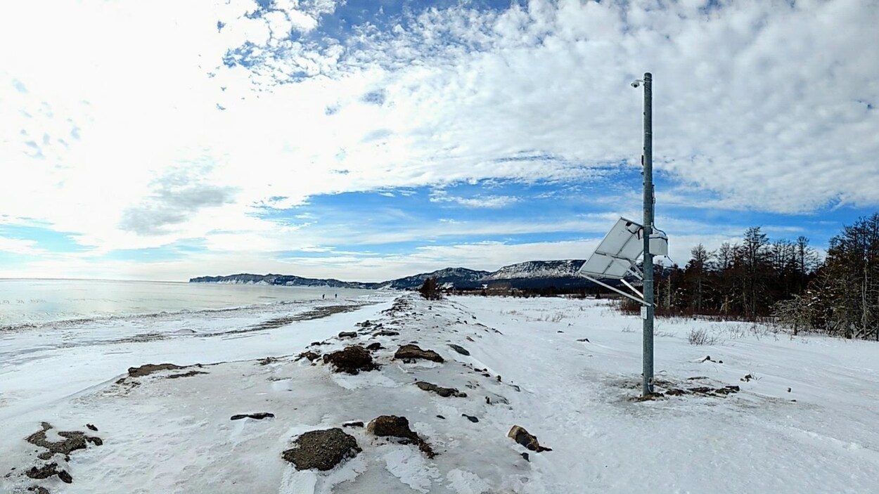 Des équipements de mesure sont installés sur un poteau près d'une berge enneigée.
