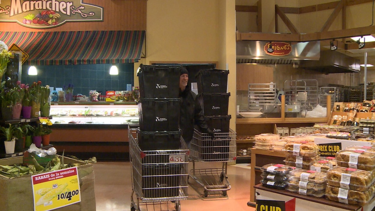 Un homme entre deux paniers d'épiceries remplis de caisses noires dans un supermarché.