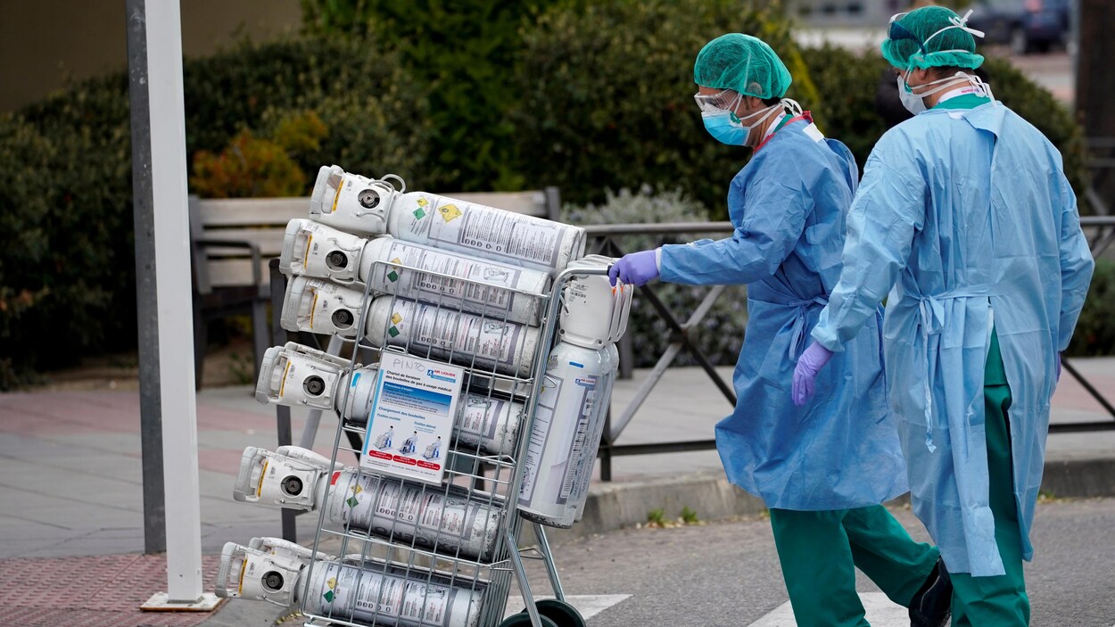 Deux personnes portant gants et masques transportent les bonbonnes sur un chariot.