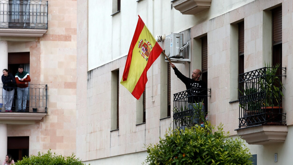 Un homme agite un drapeau espagnol à son balcon.