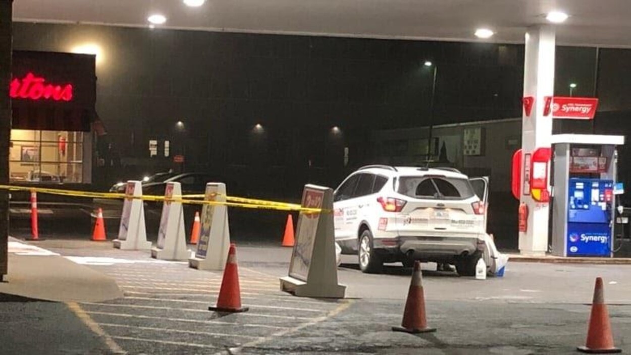 Une station de services avec une voiture arrêté et des cones oranges.