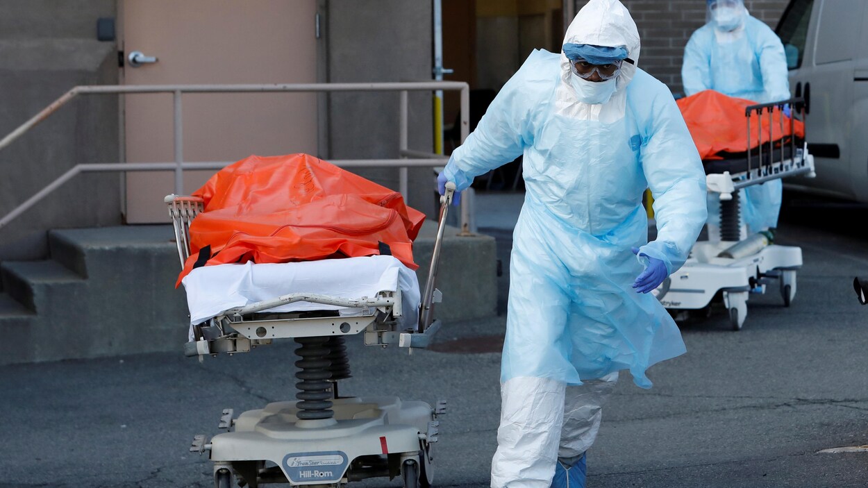 Un travailleur de la santé tire un lit d'hôpital sur lequel se trouve le corps d'une personne tuée par la COVID-19.