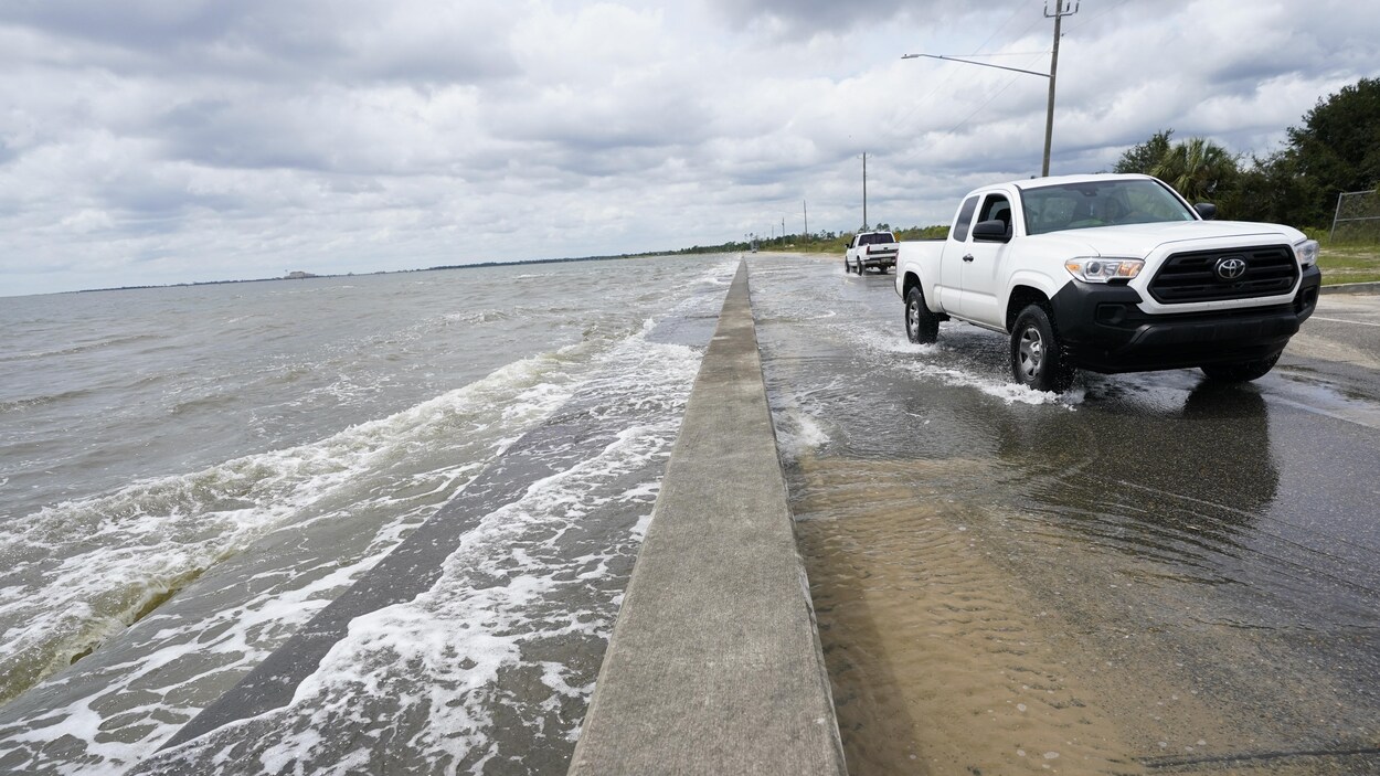 Les eaux du golfe du Mexique inondent partiellement une route sur laquelle circulent des voitures.