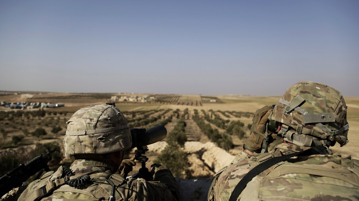 Deux soldats américains installés en hauteur regardent au loin, à l'aide de jumelles, le village de Manbij, au nord de la Syrie.