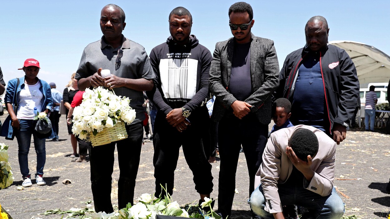 Des gens se recueillent devant des fleurs et des photos.