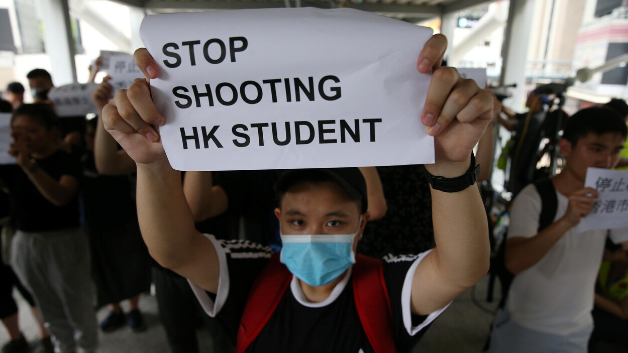 Un homme brandit une pancarte sur laquelle on peut lire : « Arrêtez de tirer sur les étudiants de Hong Kong ».