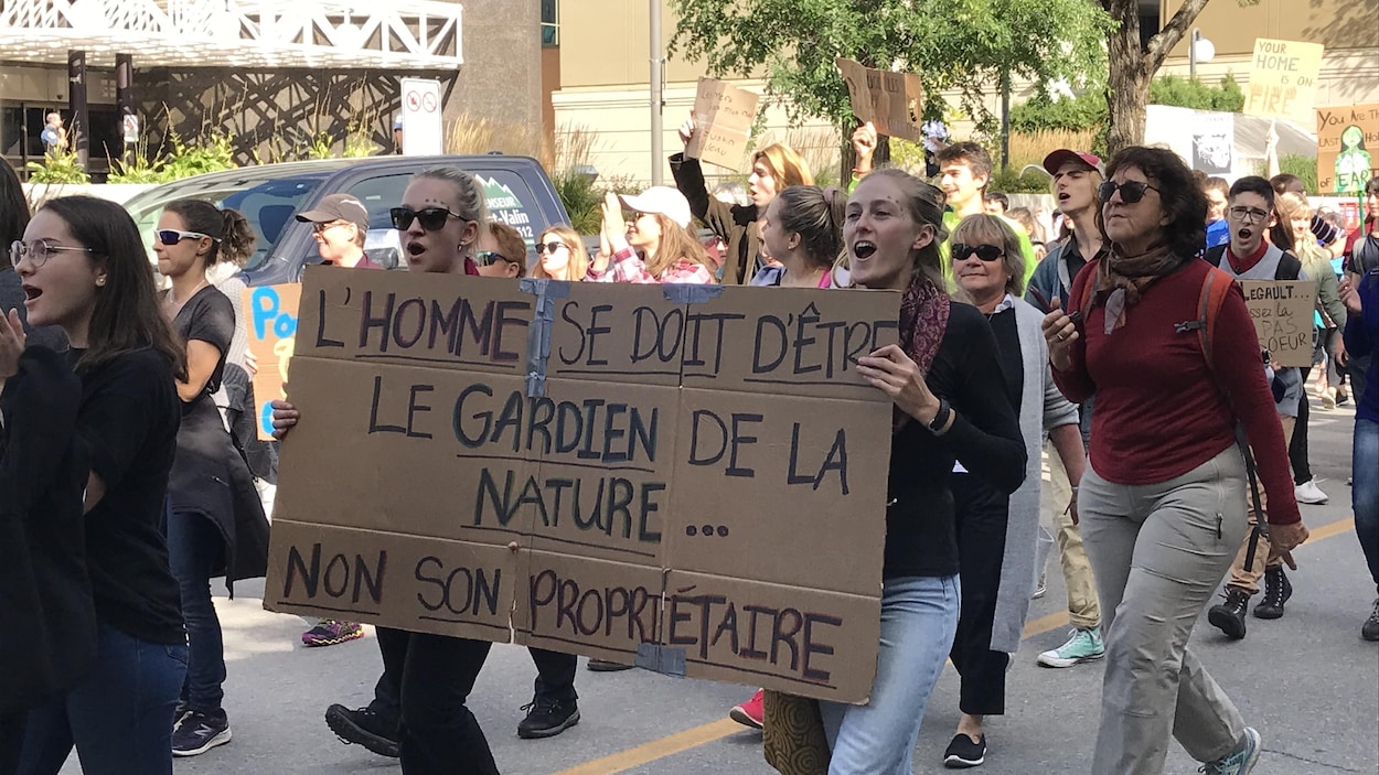 Des manifestants pour le climat avec une pancarte sur lequel il est écrit L'homme se doit d'être le gardien de la nature... non son propriétaire.
