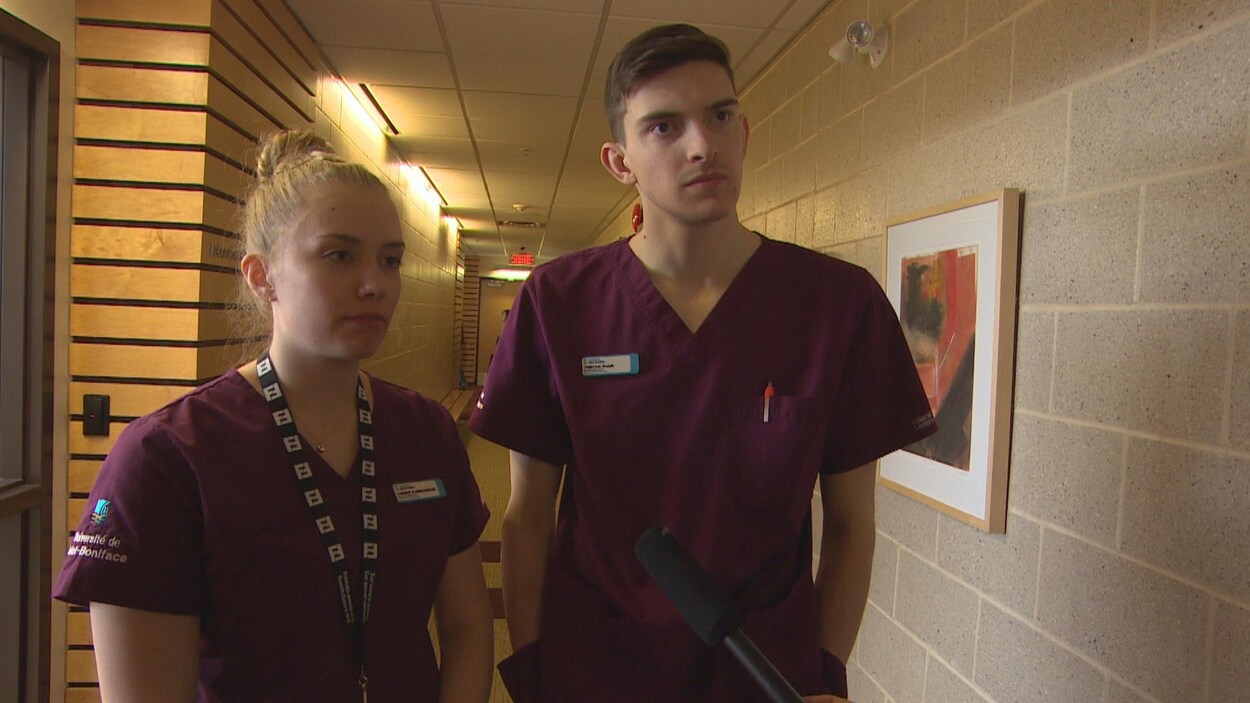 Deux jeunes gens, un homme et une femme, sont debout dans un couloir.