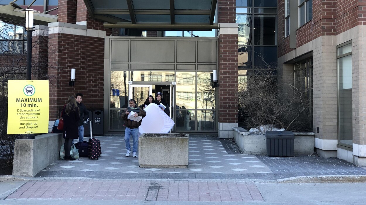 Plusieurs personnes sortent d'un bâtiment de l'Université d'Ottawa avec des caisses et des valises.