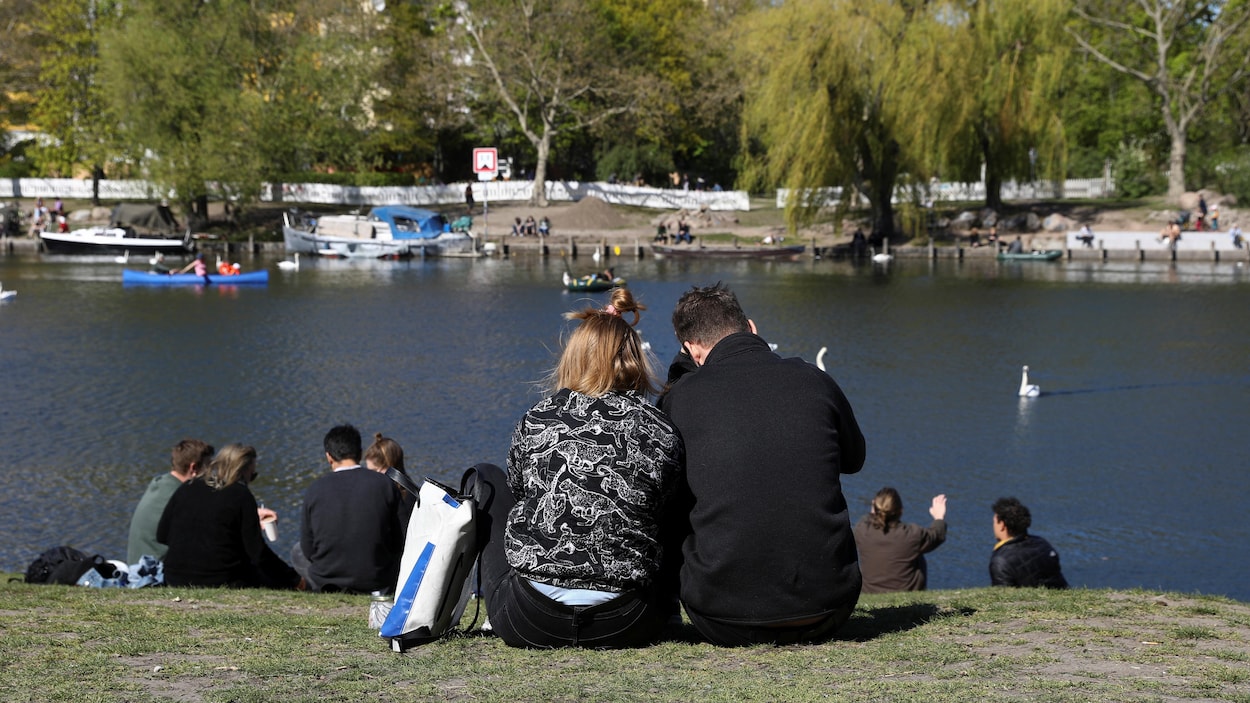 Des gens s'assoient au soleil près de la rivière Landwehrkanal à Berlin, Allemagne, le 19 avril 2020.