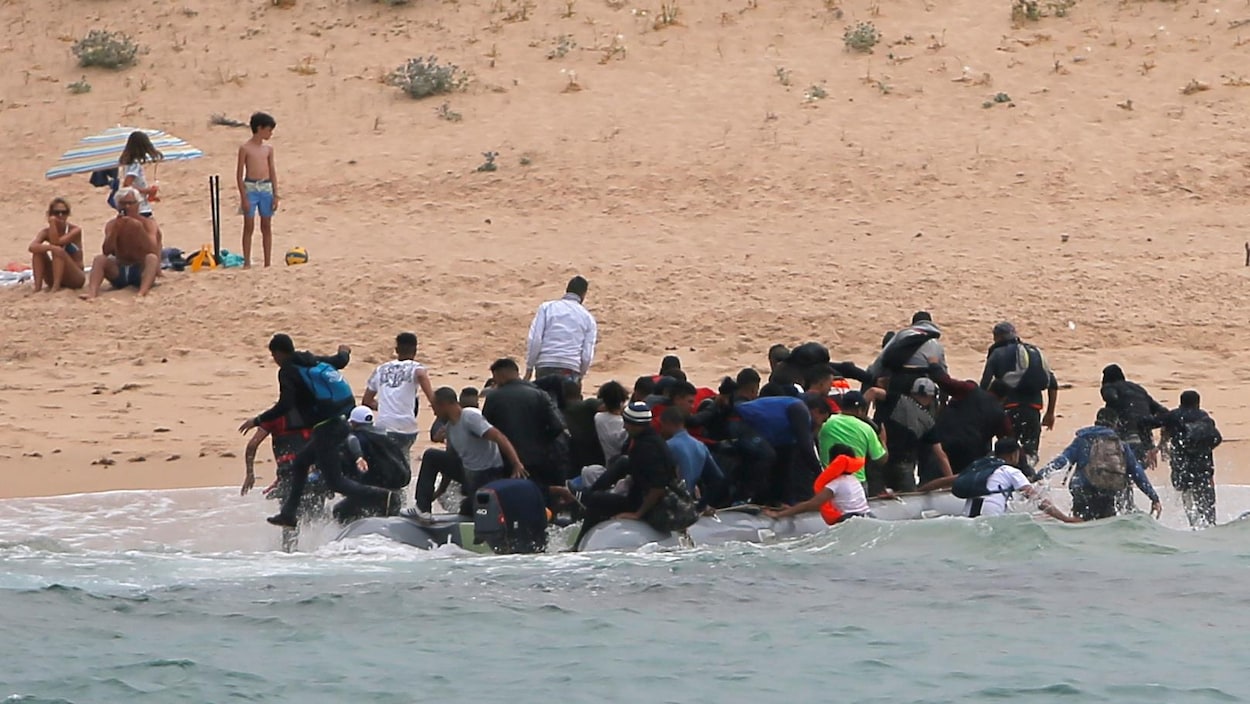 Des gens débarquant d'un bateau sur une plage devant des baigneurs.