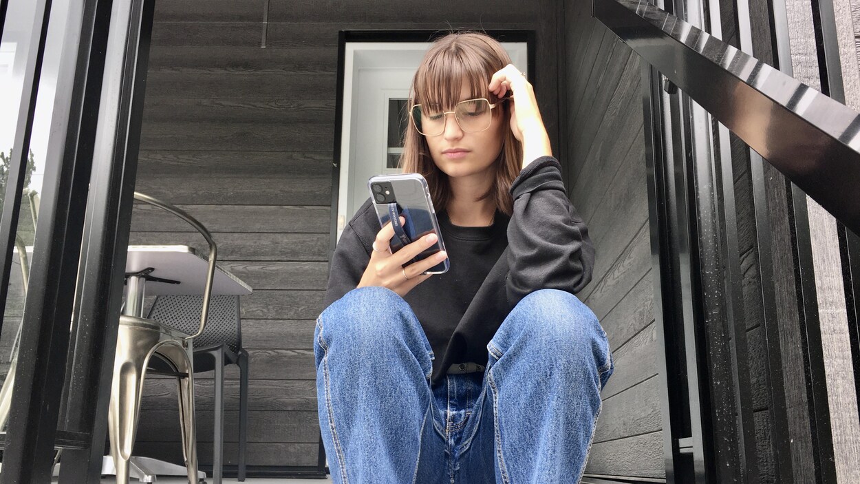 Un femme est assise dans les escaliers devant une maison et regarde son cellulaire.