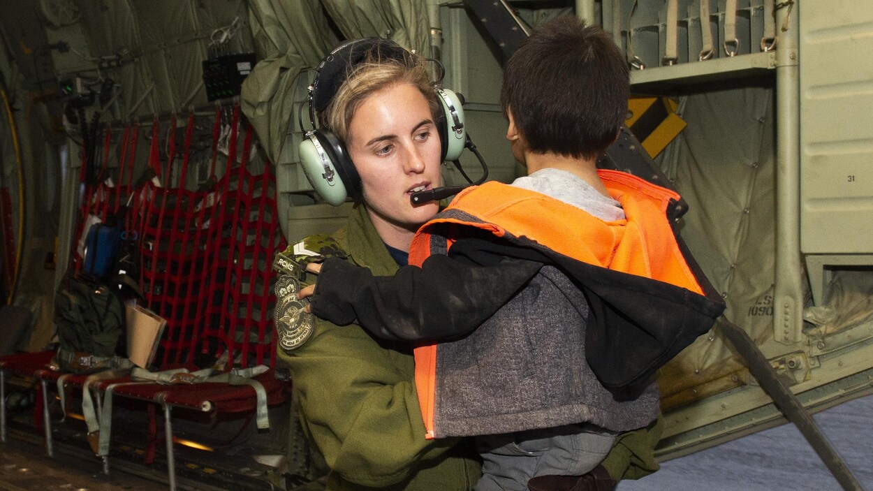 Une militaire porte un enfant évacué pour le faire descendre de l'avion.