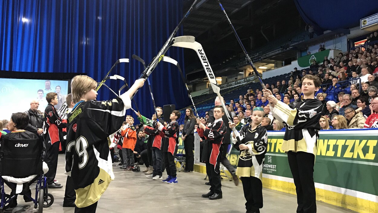 Des dizaines de jeunes tiennent des bâtons de hockey dans l’air pour permettre à la famille de traverser. Des dizaines de jeunes tiennent des bâtons de hockey dans l’air pour permettre à la famille de traverser.