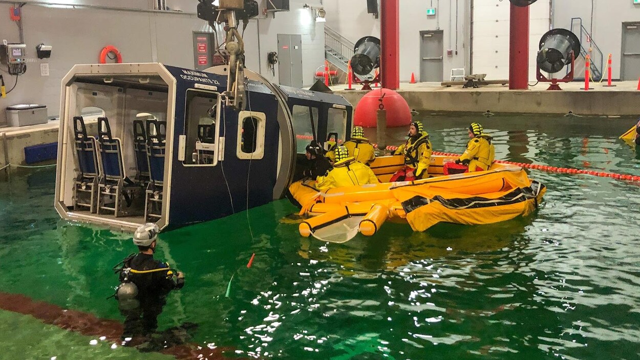 Quatre personnes dans un canot gonflable et deux plongeurs lors d'un exercice de survie dans une piscine.