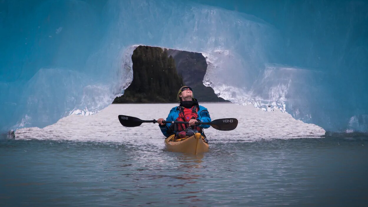 Un homme sur un kayak la tête versée vers l'arrière pour regarder la glace au-dessus de lui.