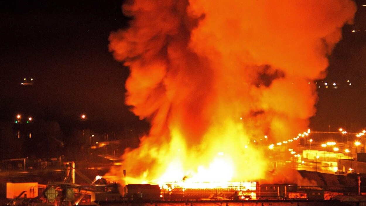 Des flammes et de la fumée provenant d'un édifice en feu s'élancent vers le ciel la nuit.
