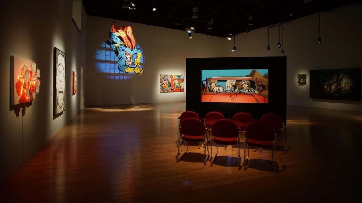 Une salle dans un musée avec de grandes peintures illuminées sur des murs et sur des panneaux.