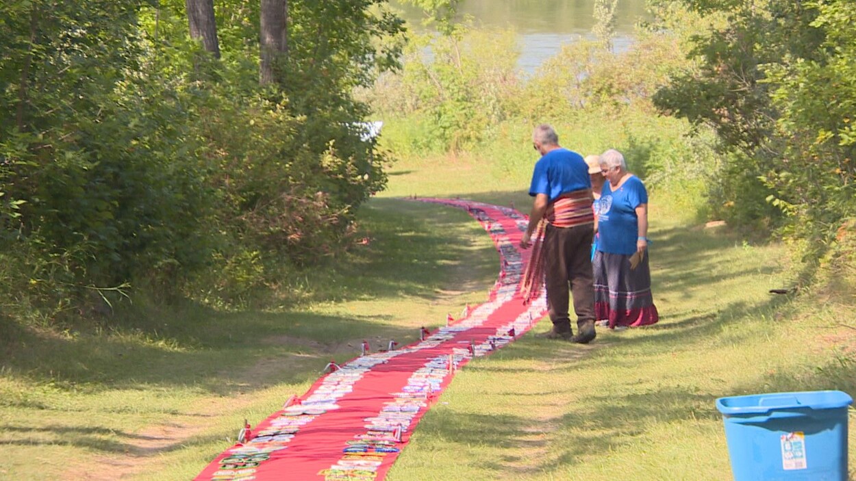 Deux femmes et un homme debout près d'un long tapis rouge installé sur le gazon.