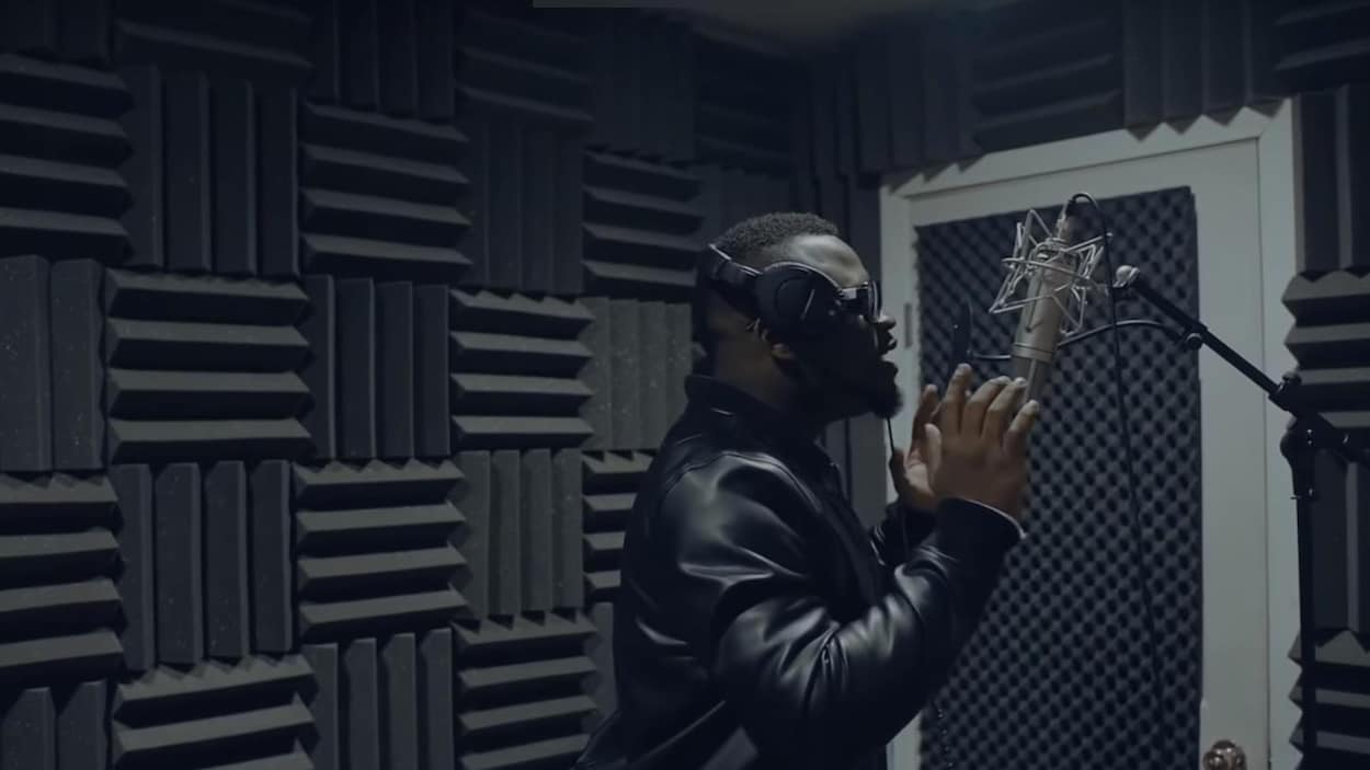 Un artiste chante devant un microphone, dans un studio insonorisé.