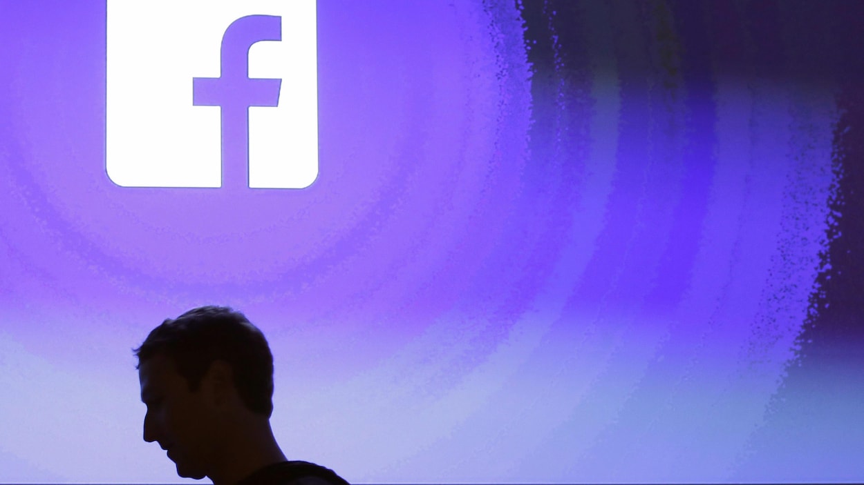 Mark Zuckerberg de profil devant le logo de sa compagnie Facebook