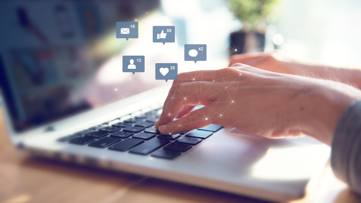 Une personne tape sur le clavier d'un ordinateur et des émoticônes apparaissent sur la photo.