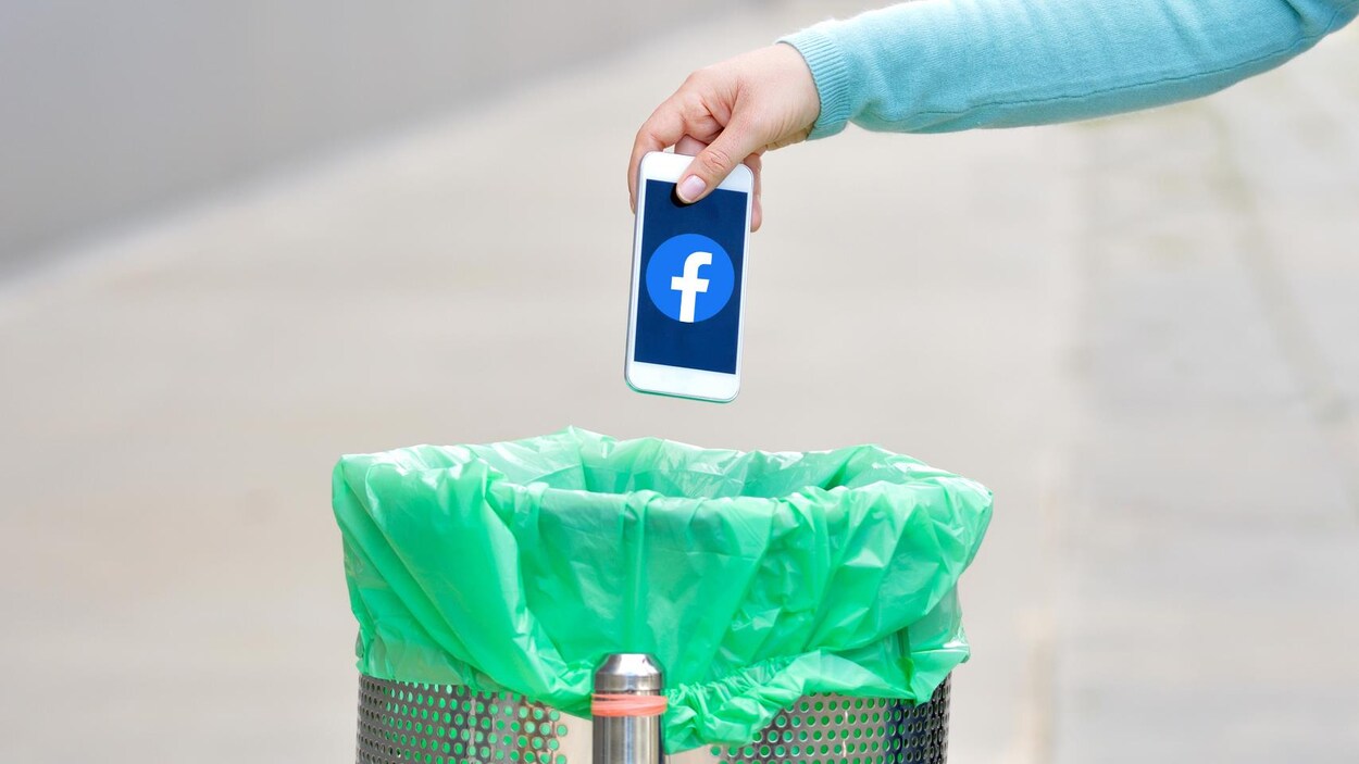 Une personne jette un téléphone cellulaire avec le logo de Facebook à la poubelle.