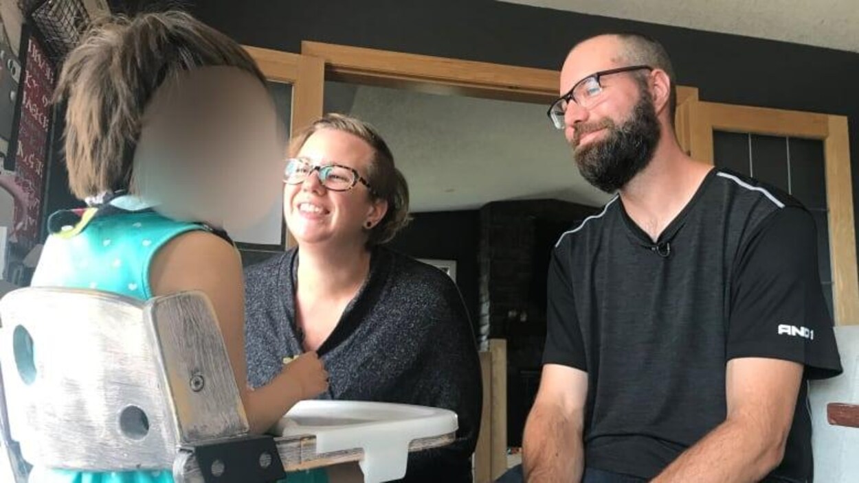 Deux parents regardent d'un oeil attendri une petite fille assise de dos dans une chaise pour enfants.