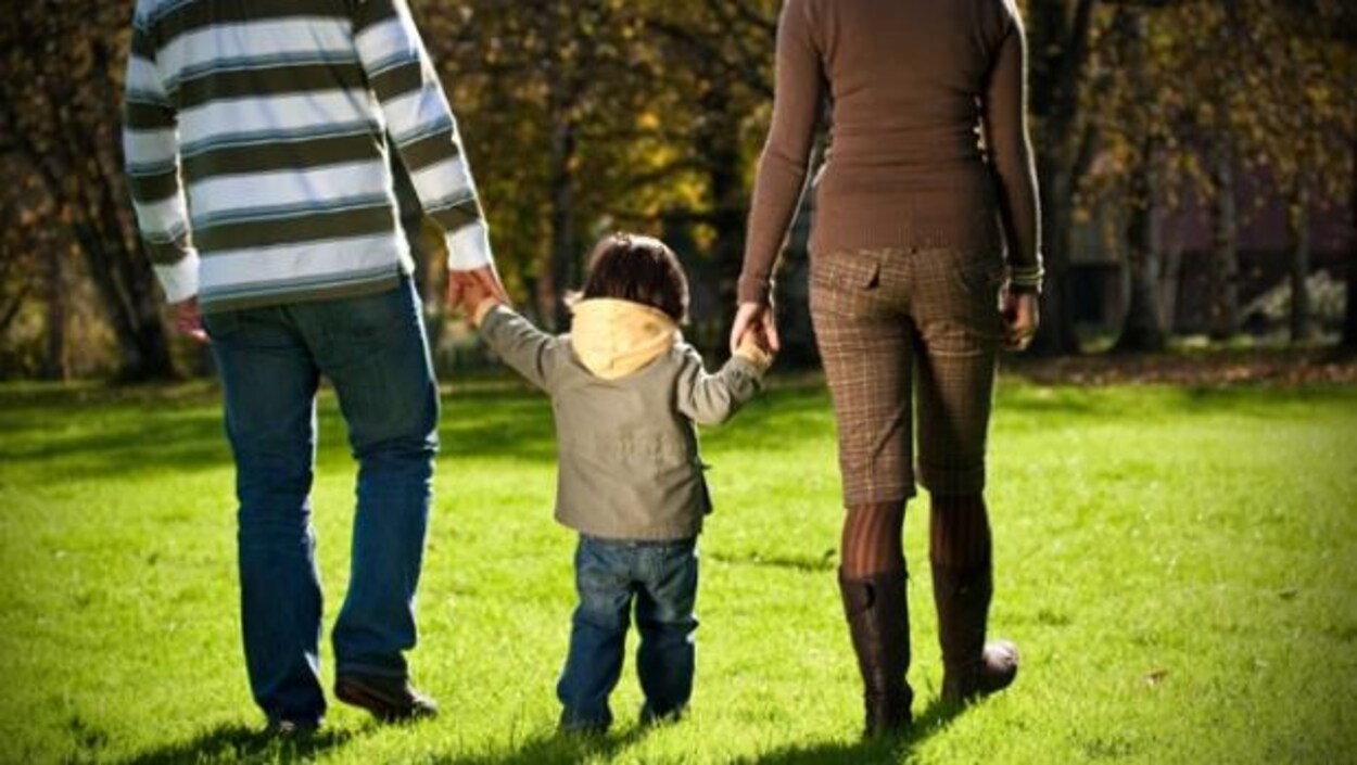 Un homme et une femme tiennent chacun la main d'en enfant, en marchant, dos à la caméra.