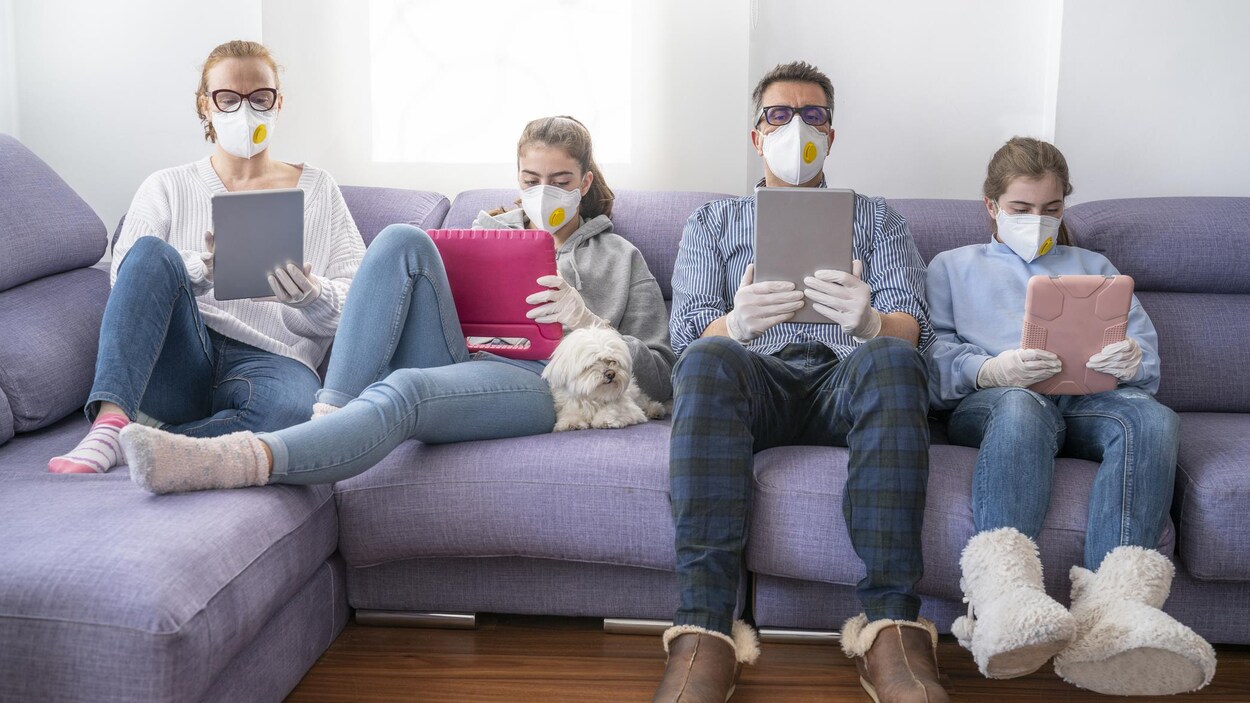 Une mère, un père et deux adolescents portant des masques devant leurs tablettes.