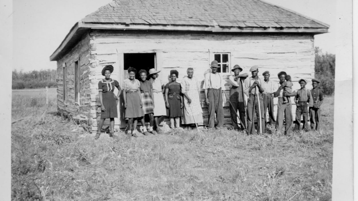 Des pionniers noirs devant un bâtiment relativement bas en rondin de bois.