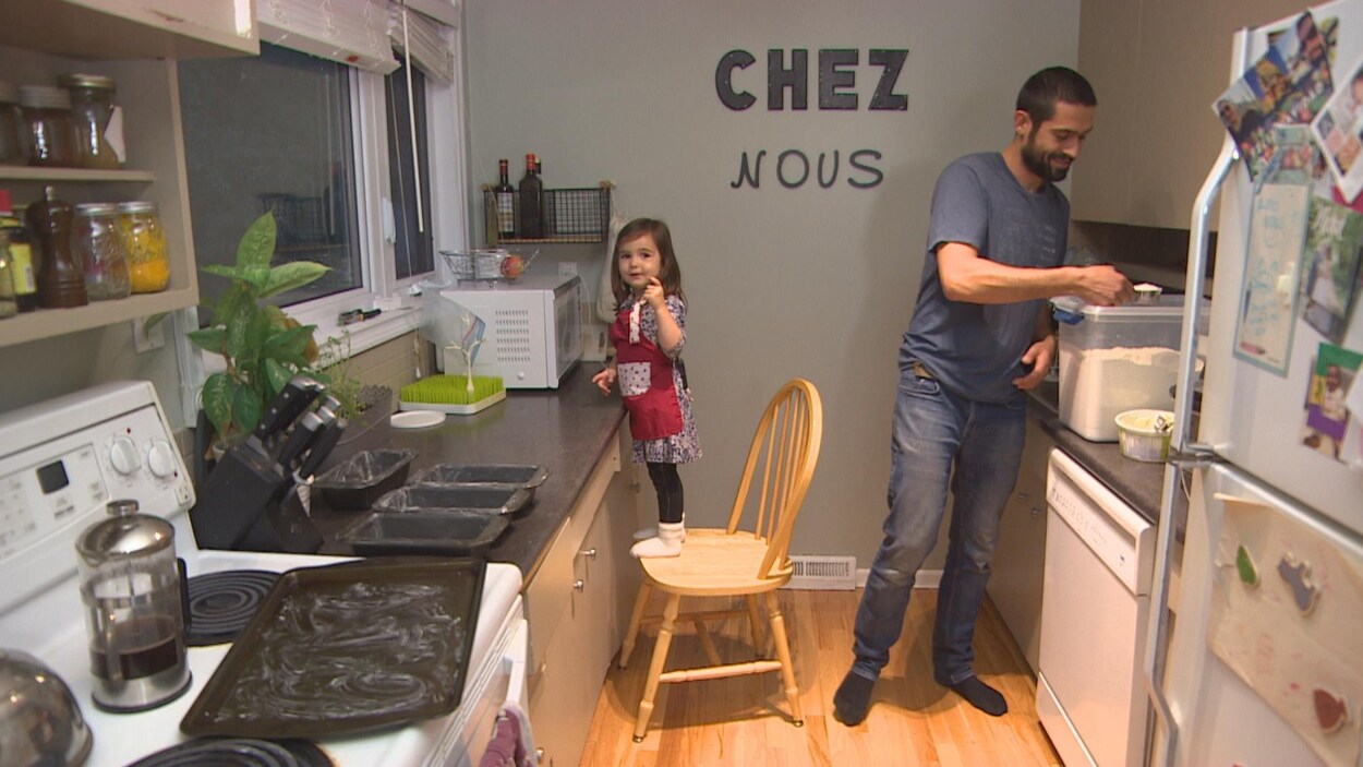 Patrick Lessard prend de la farine dans un contenant transparent et Alizée est debout sur une chaise.