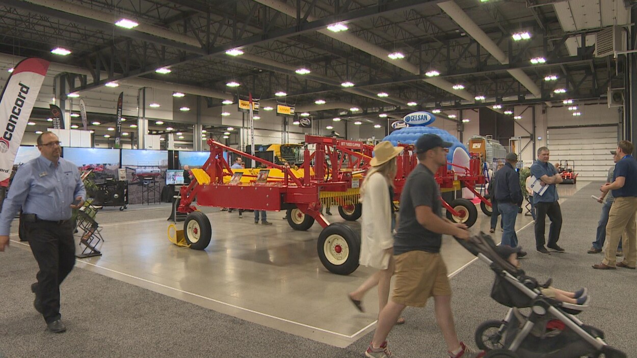 Des visiteurs à la foire agricole marchent près de machines agricoles exposées à l’intérieur d’un bâtiment à la Place Evraz.