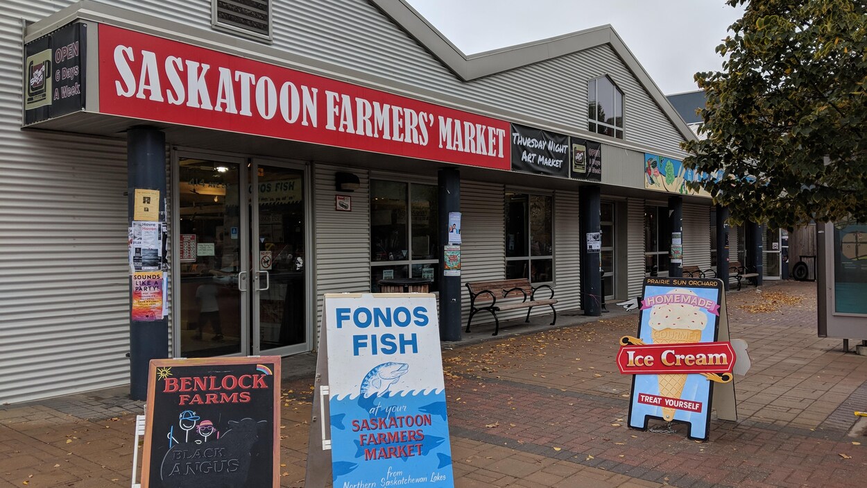 Devanture de l'édifice du marché des fermiers de Saskatoon avec des pancartes commerciales, sous un ciel gris.