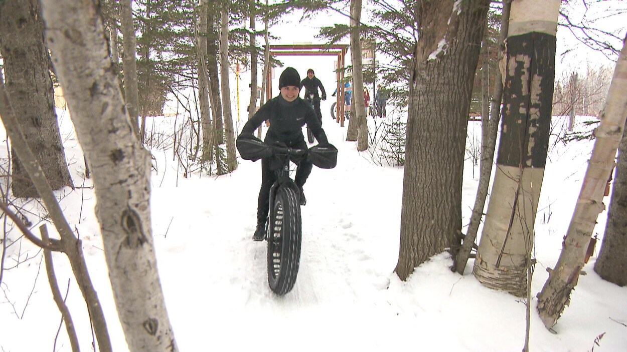 Une jeune femme sourit sur un fatbike dans un sentier.