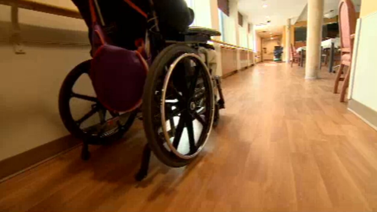 Une personne assise dans un fauteuil roulant dans un couloir d'un centre de soin longue durée. Une personne assise dans un fauteuil roulant dans un couloir d'un centre de soin longue durée.