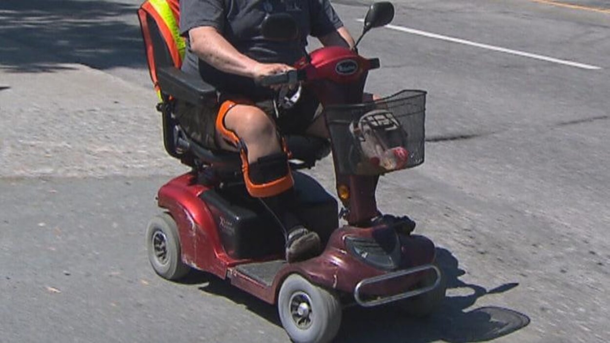 Un homme se déplace en fauteuil roulant motorisé le long d'une route Un homme se déplace en fauteuil roulant motorisé le long d'une route