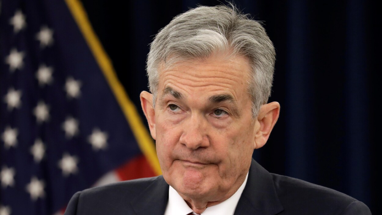 Le président de la Réserve fédérale américaine, Jerome Powell est assis et regarde vers le haut. Un drapeau américain est accroché derrière lui.