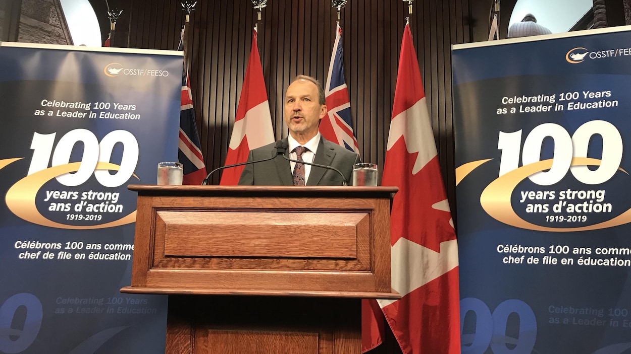 Harvey Bischof parle aux médias sur un podium.