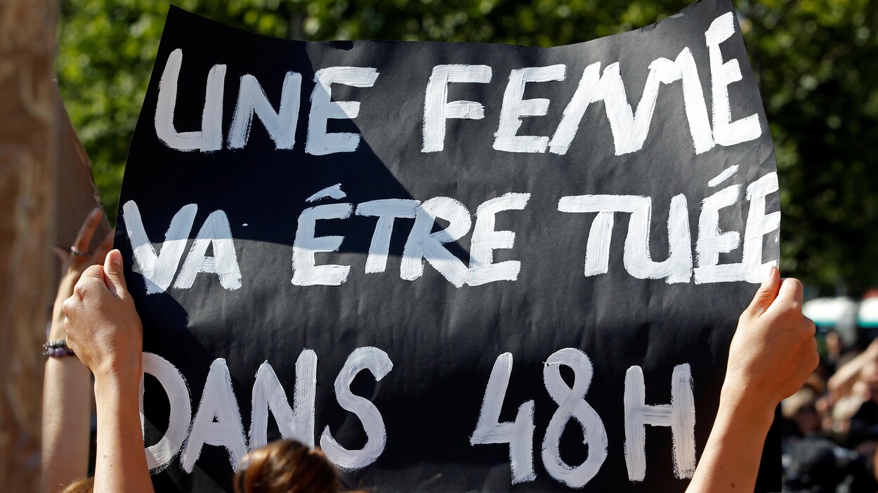 Des mains brandissent une affiche noire avec lettres blanches.