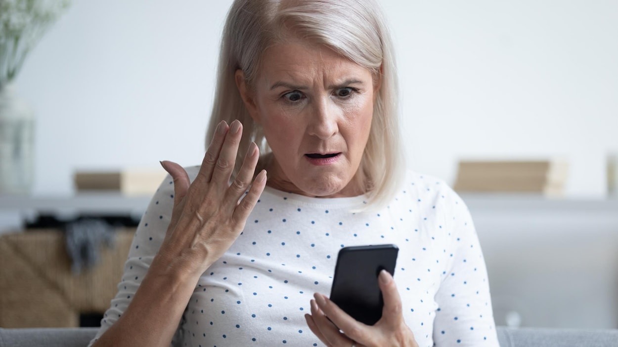 Une femme est exaspérée en regardant son cellulaire.